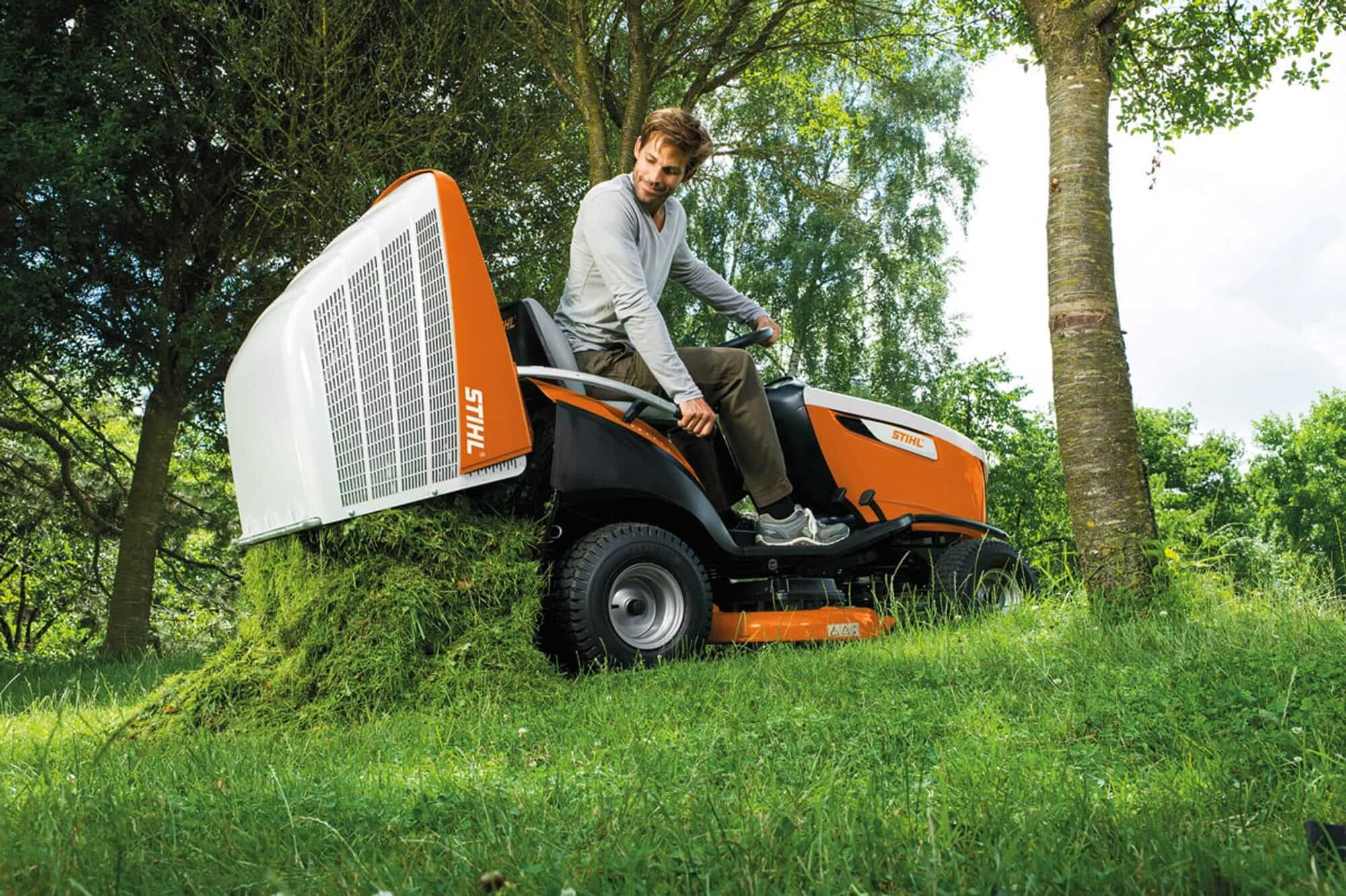 A person using a STIHL ride-on lawnmower to maintain a grassy area surrounded by trees.
