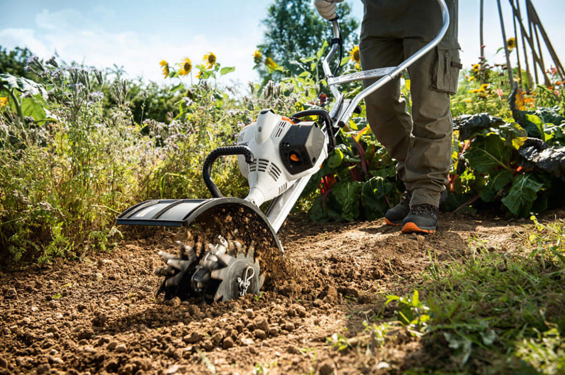 Person using a STIHL Multi Engine tiller in a garden, perfect for tree surgeons and outdoor gardening tasks.