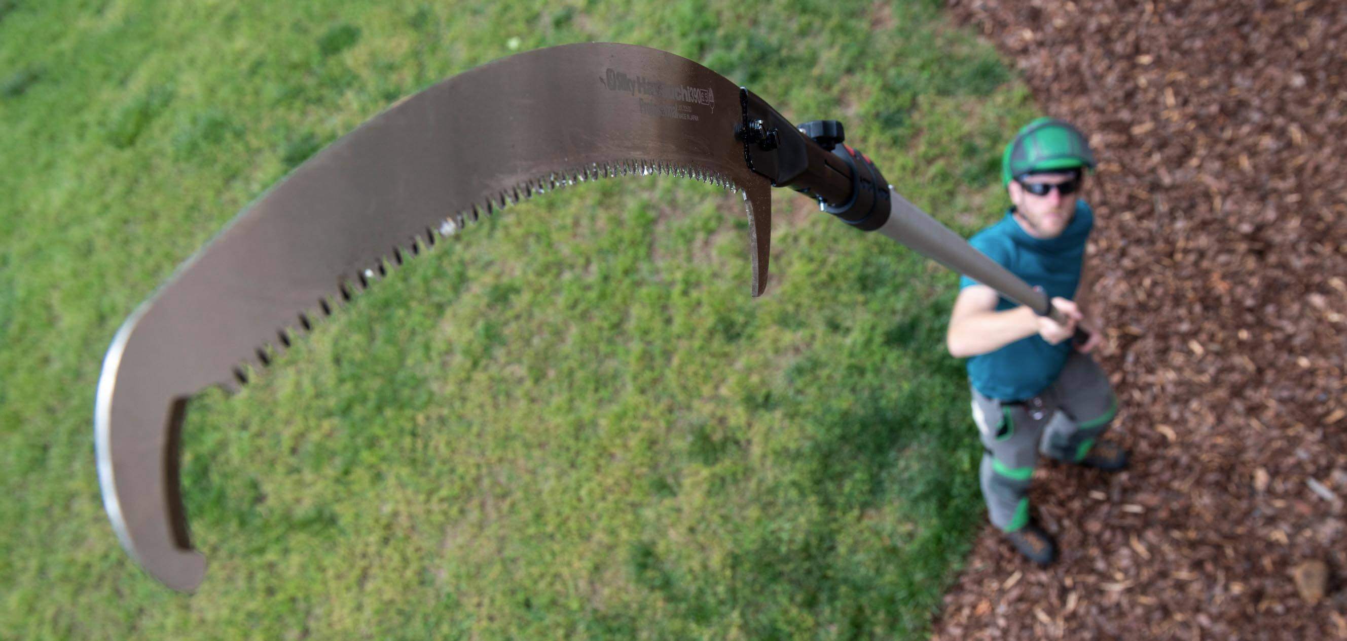 Manual pole saw held by a tree surgeon, showcasing its curved blade for efficient pruning of high branches.