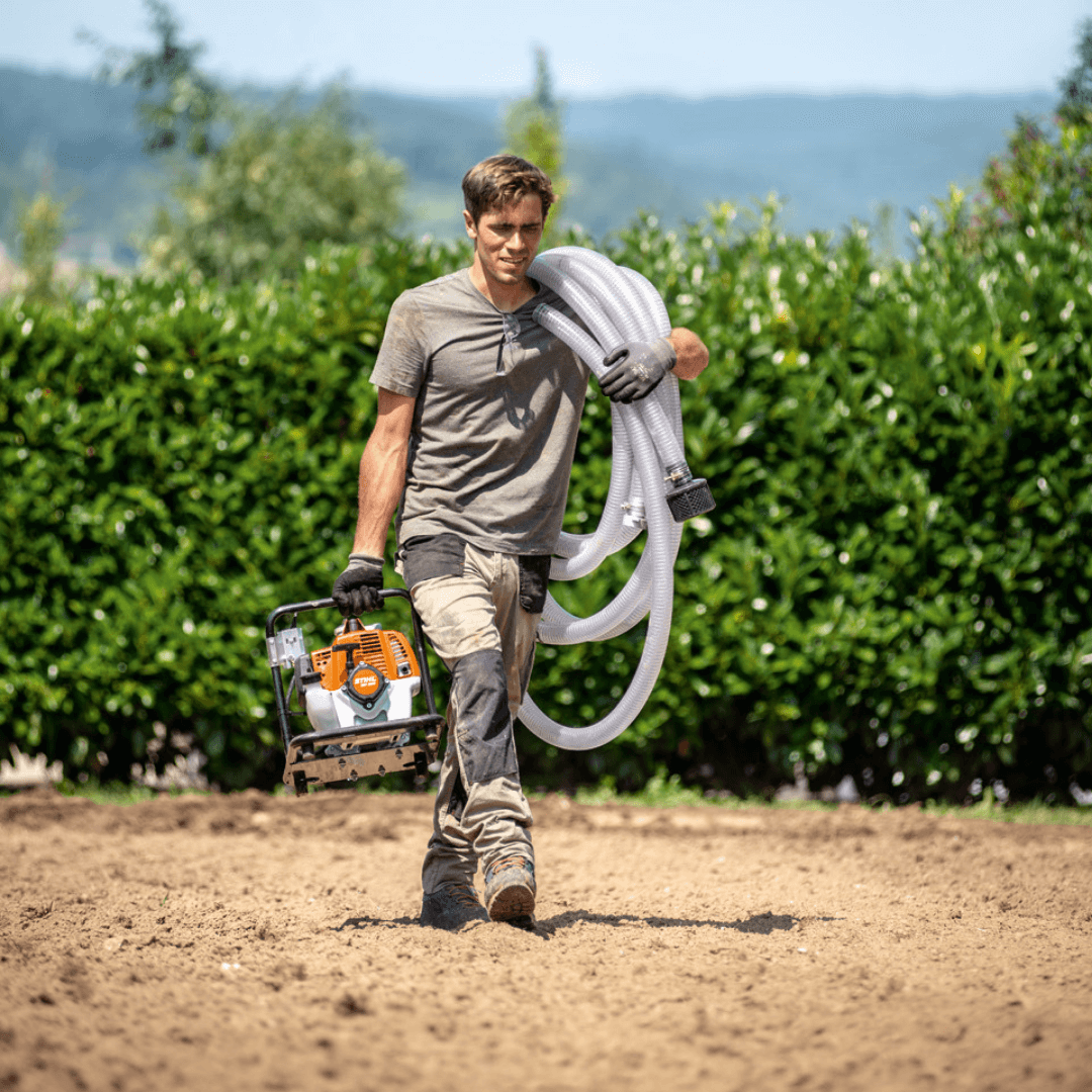 A tree surgeon carrying a STIHL water pump and hoses, ready for effective water management in the garden.