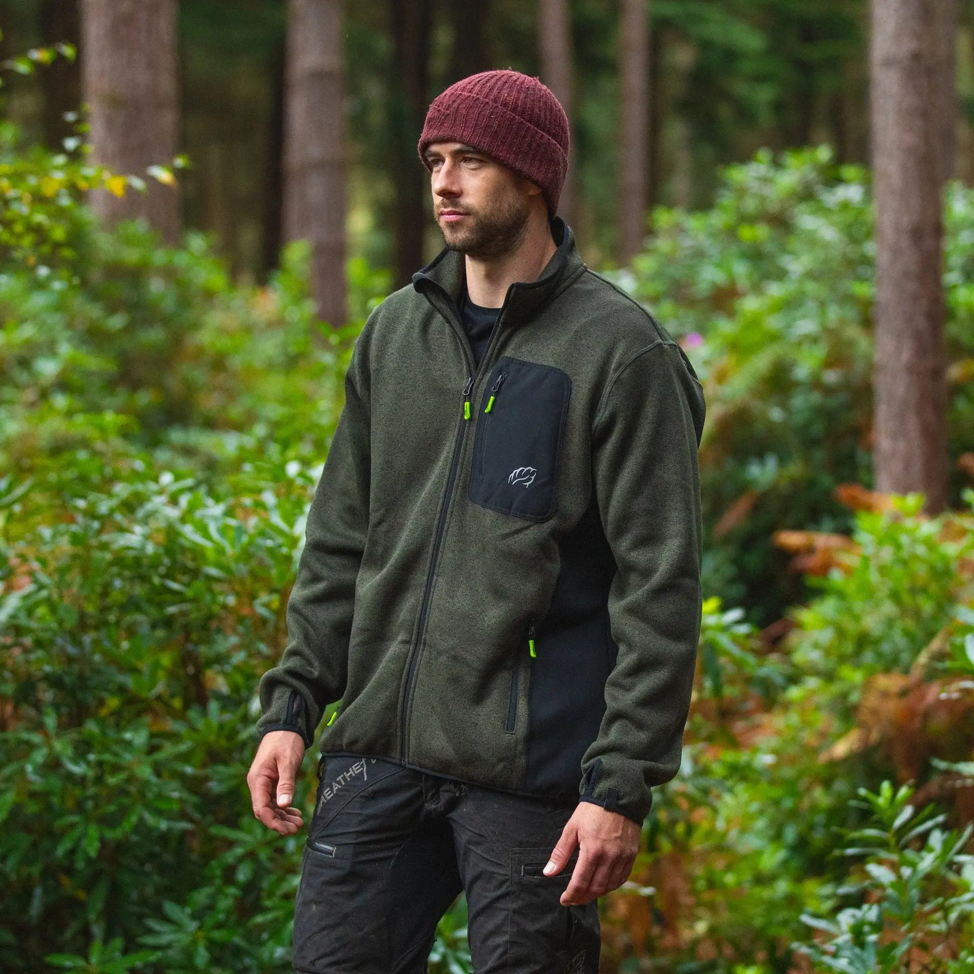 Man wearing an olive green zip-up hoodie in a forest, perfect for tree surgeons and outdoor enthusiasts.