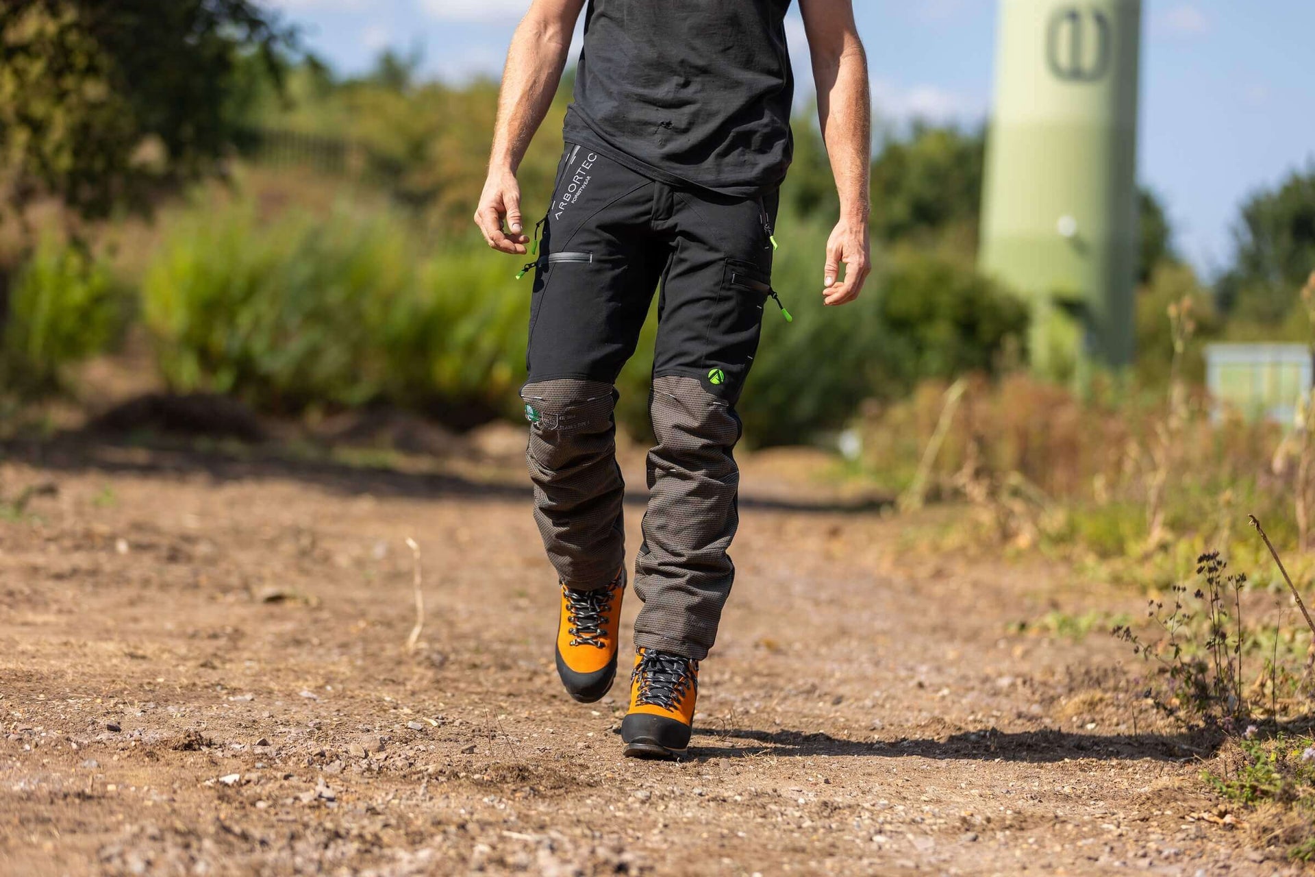 Man walking in Arbortec clothing and boots, showcasing durability for tree surgeons in a forested area.