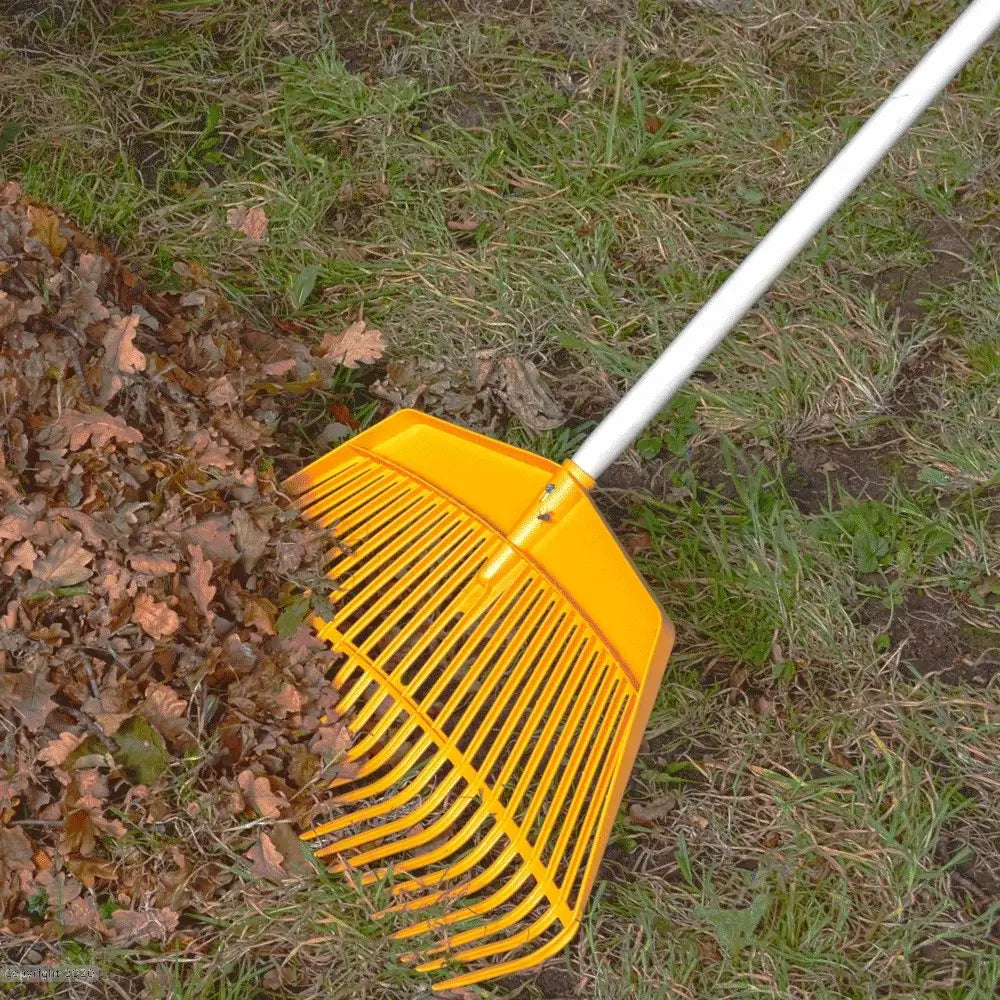 Yellow garden rake on grass next to a pile of autumn leaves, ideal for tree surgeons and gardening enthusiasts.
