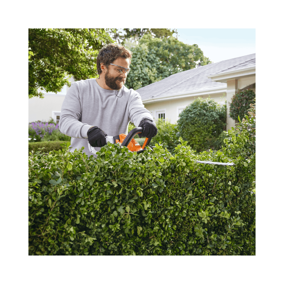 Man using HSA 40 Cordless Hedge Trimmer 20" to trim lush green hedge in a residential garden.