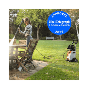 Person using RE 130 Plus Pressure Washer to clean patio furniture in a garden.