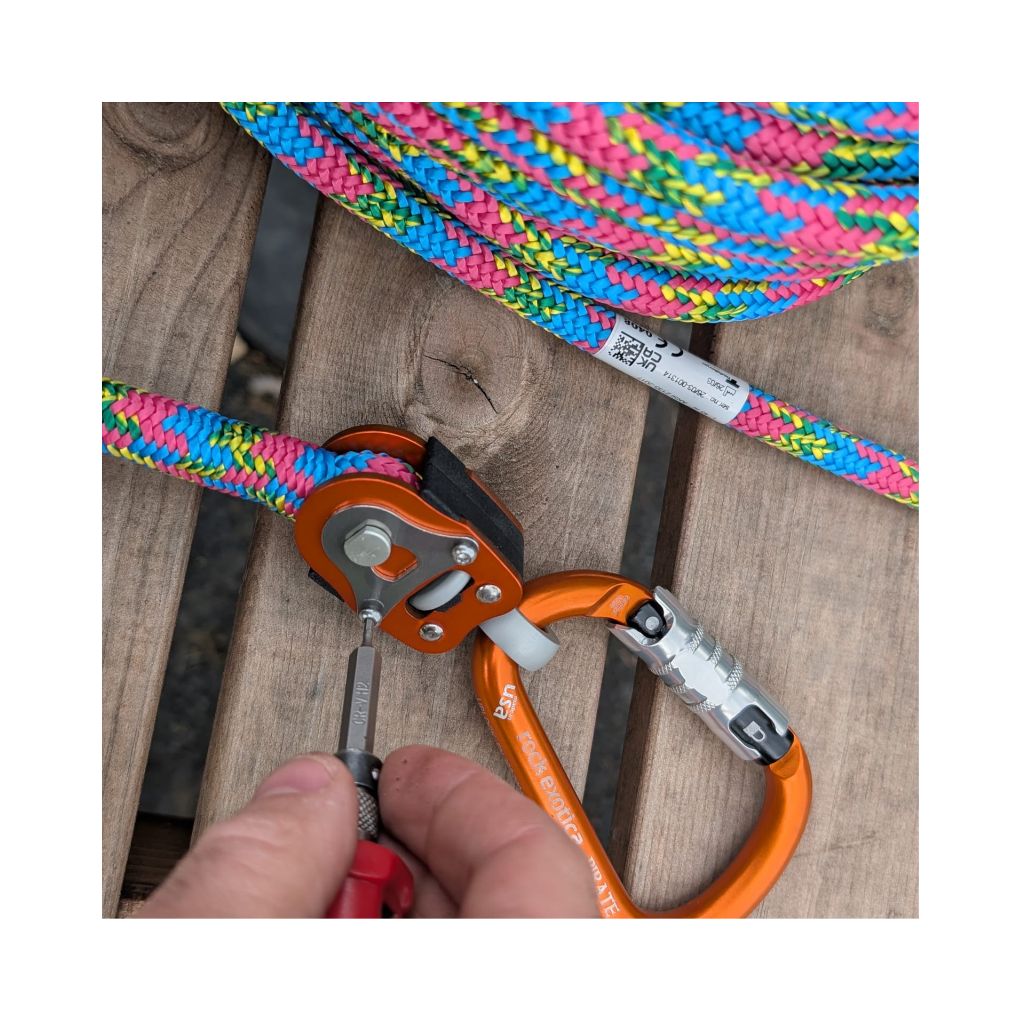 Close-up of the Omnix Swivel Eye&Pin connected to colorful climbing rope and carabiner on wooden surface.