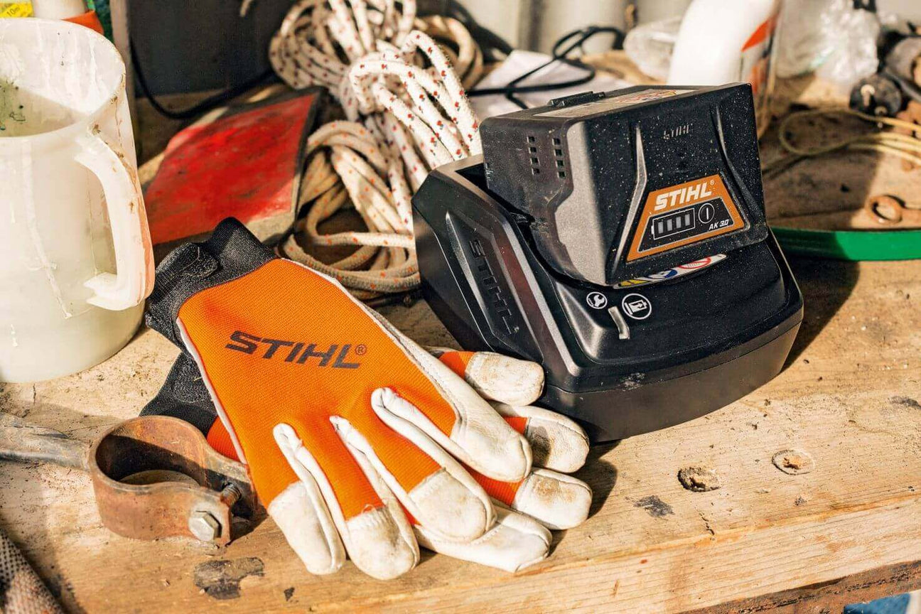 STIHL work gloves and battery charger on a wooden workbench in a workshop setting.