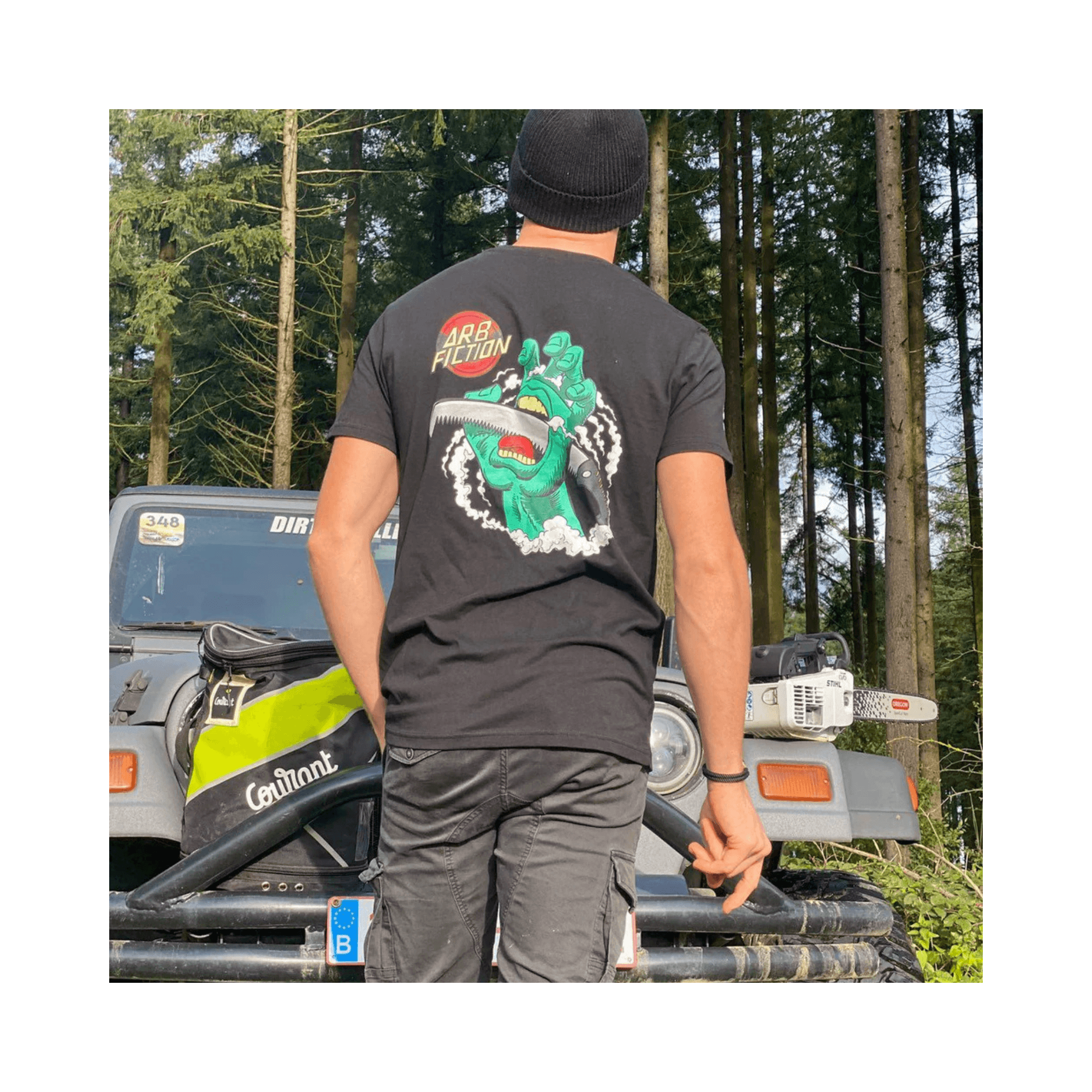 Person wearing Arb Fiction Screaming Hand T-Shirt in black, showcasing tree care culture in a forested setting.