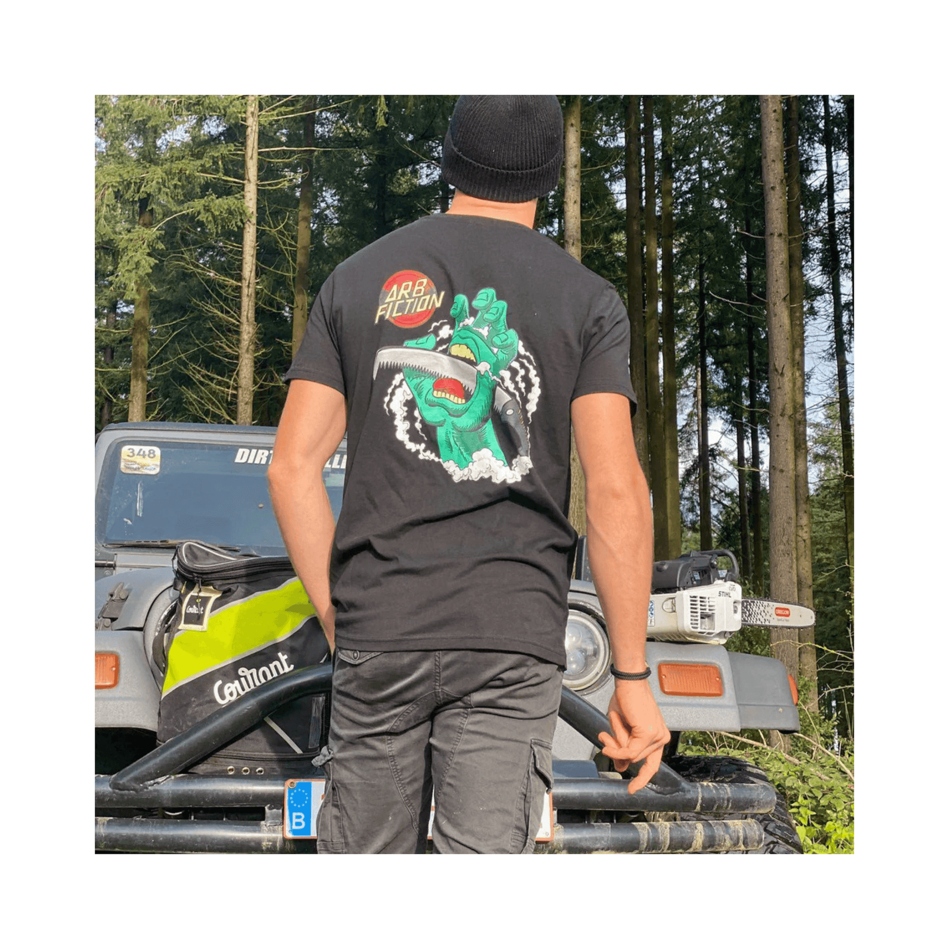 Person wearing Arb Fiction Screaming Hand T-Shirt in black, showcasing tree care culture in a forested setting.
