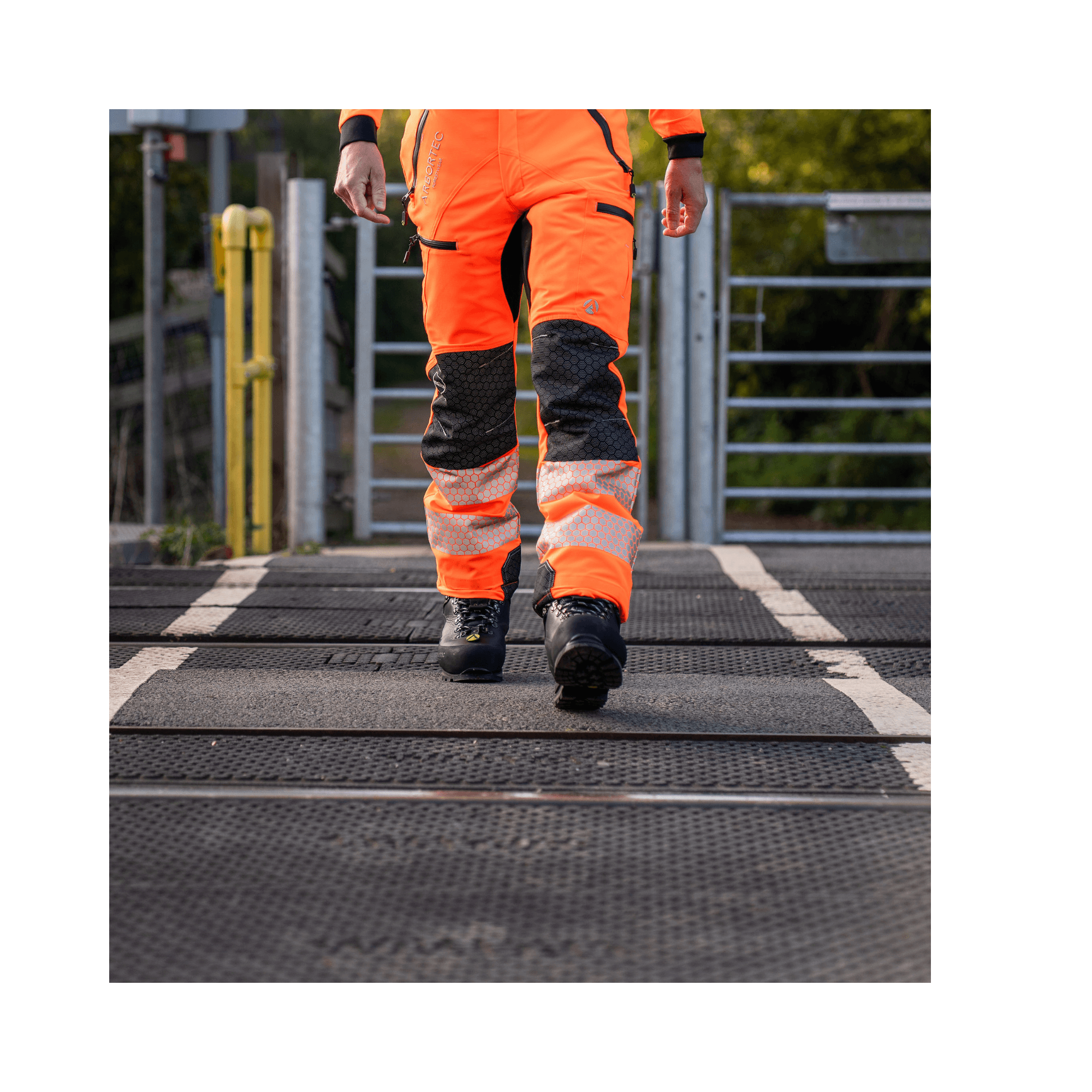 Breatheflex Pro Rail Spec Trousers Design Type C Class 2 Hi Viz Orange, worn by a worker walking on a railway platform.
