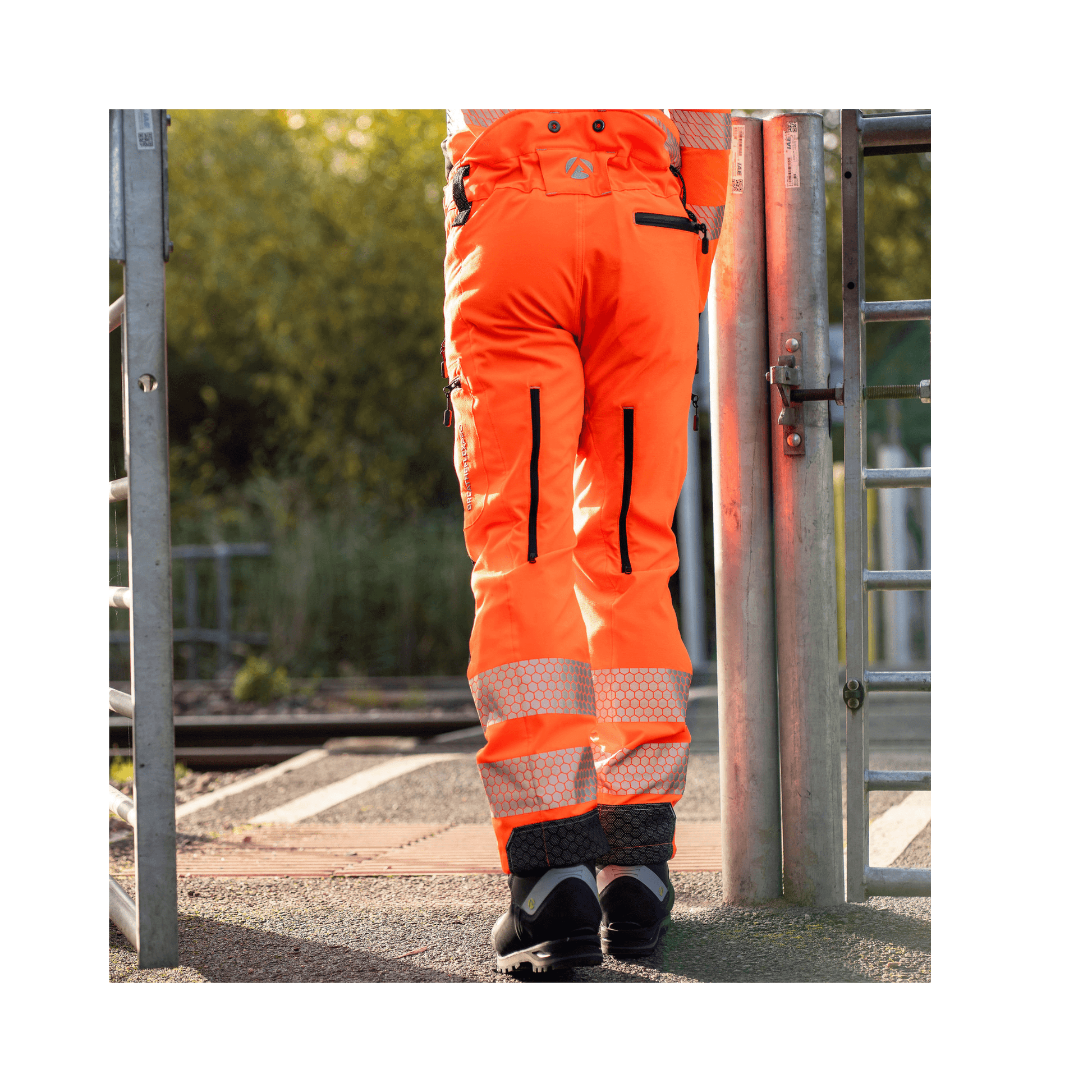 Breatheflex Pro Rail Spec Trousers Design Type C Class 2 Hi Viz Orange on a person at a rail crossing.