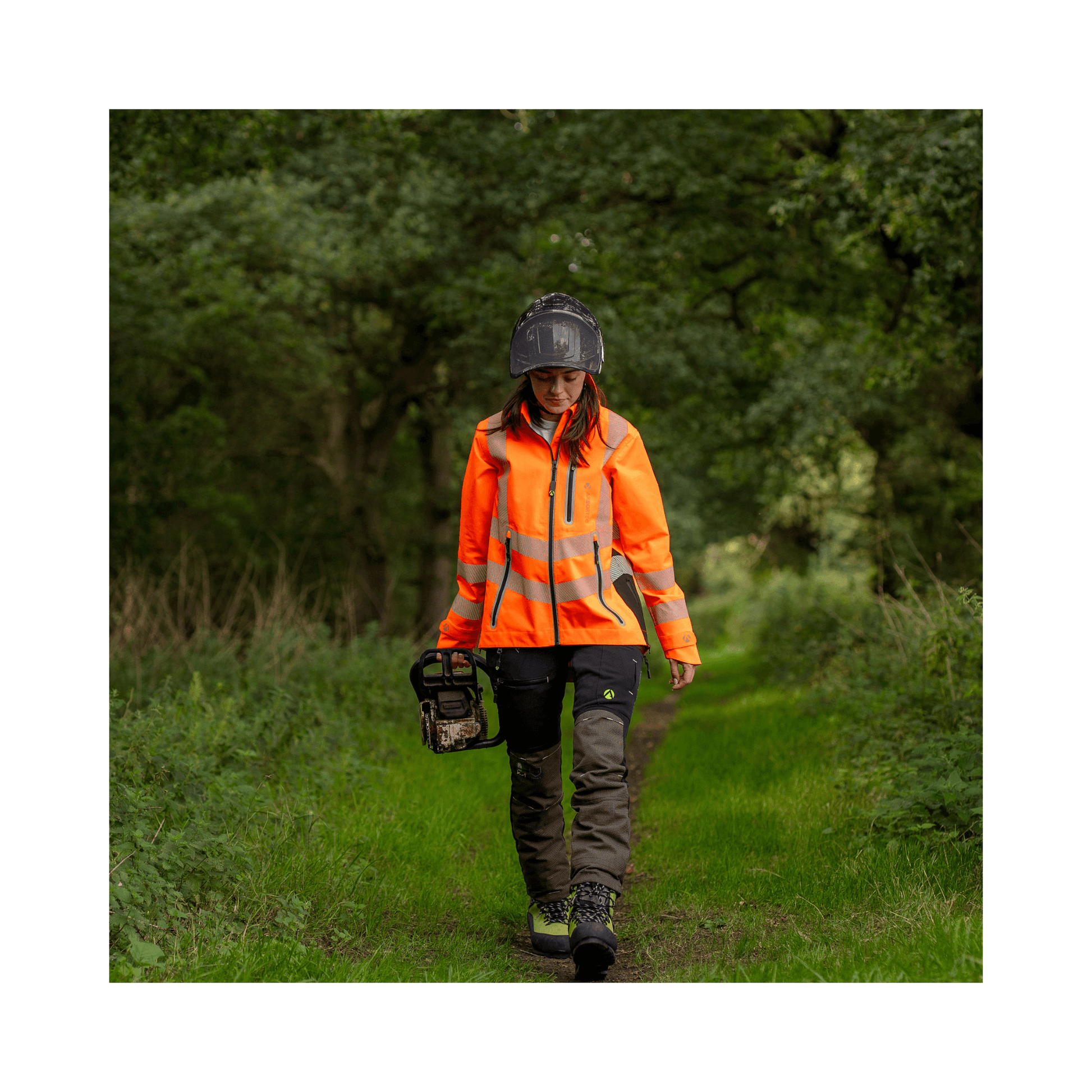 Full Zip Waterproof Womens Work Jacket Hi-Vis Orange worn by a woman walking in a green outdoor setting.