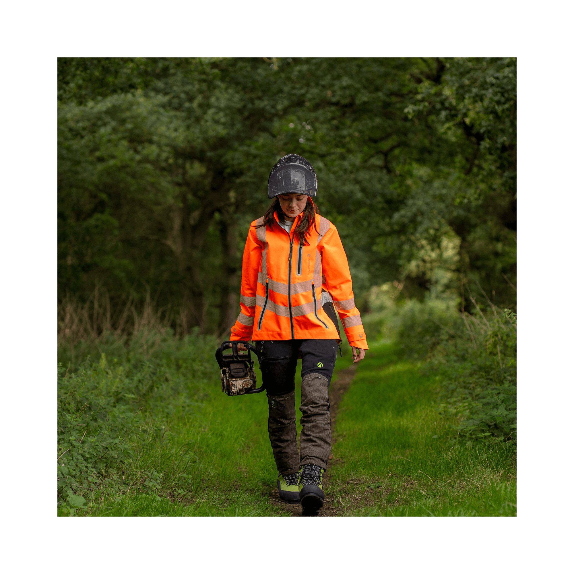 Full Zip Waterproof Womens Work Jacket Hi-Vis Orange worn by a woman walking in a green outdoor setting.