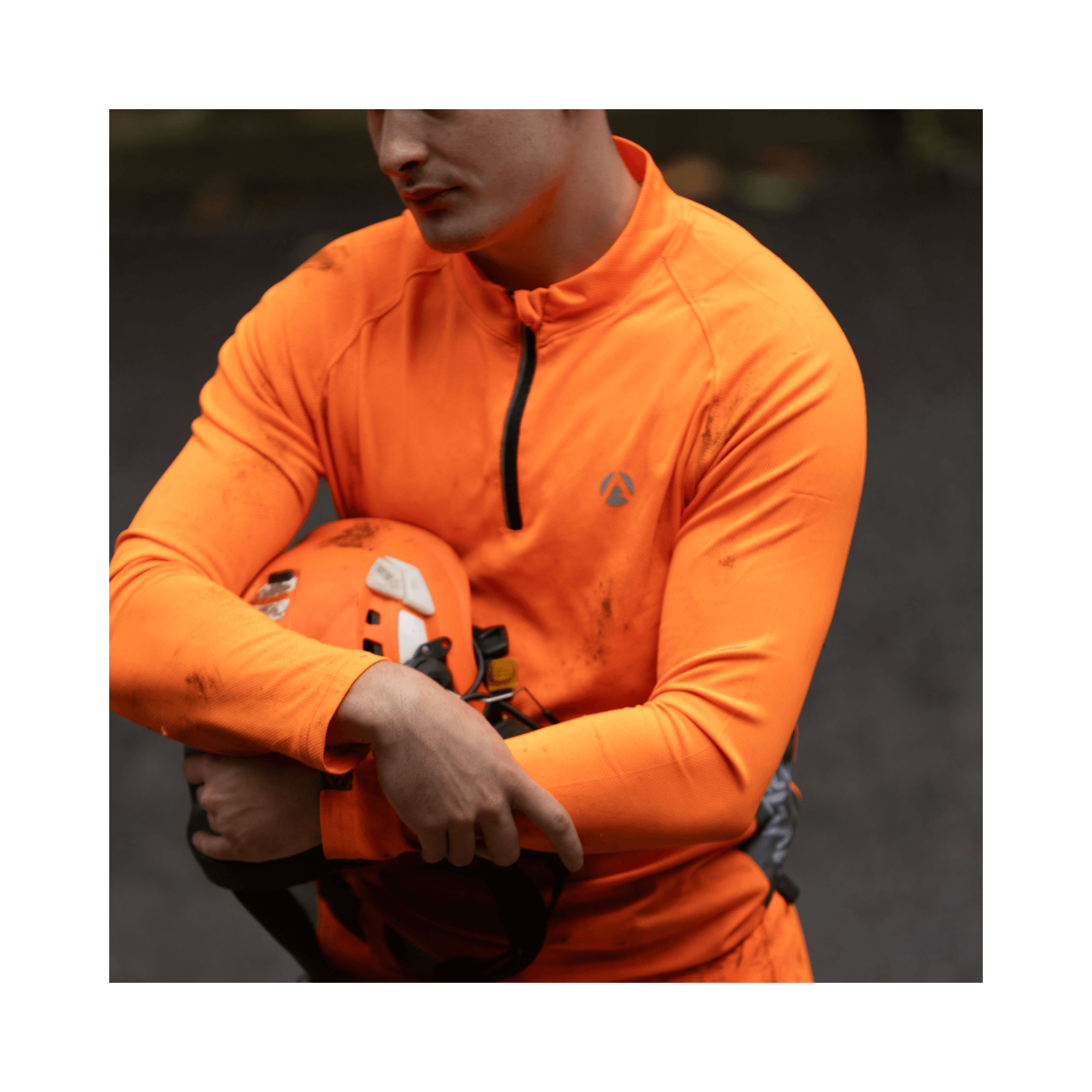 Performance T-Shirt Long Sleeve Orange worn by a person holding a helmet in an outdoor setting.