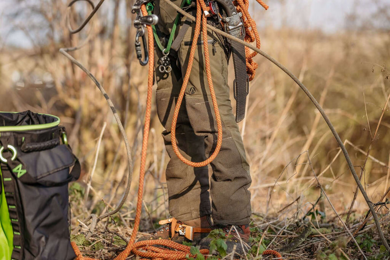 Close-up of climbing gear with ropes and harness on a person's legs outdoors in a natural setting.