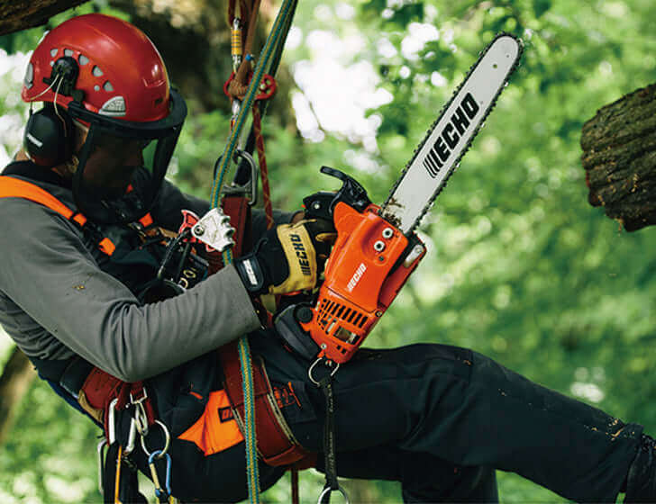 Tree surgeon using a chainsaw while climbing a tree, showcasing professional arborist skills in action.