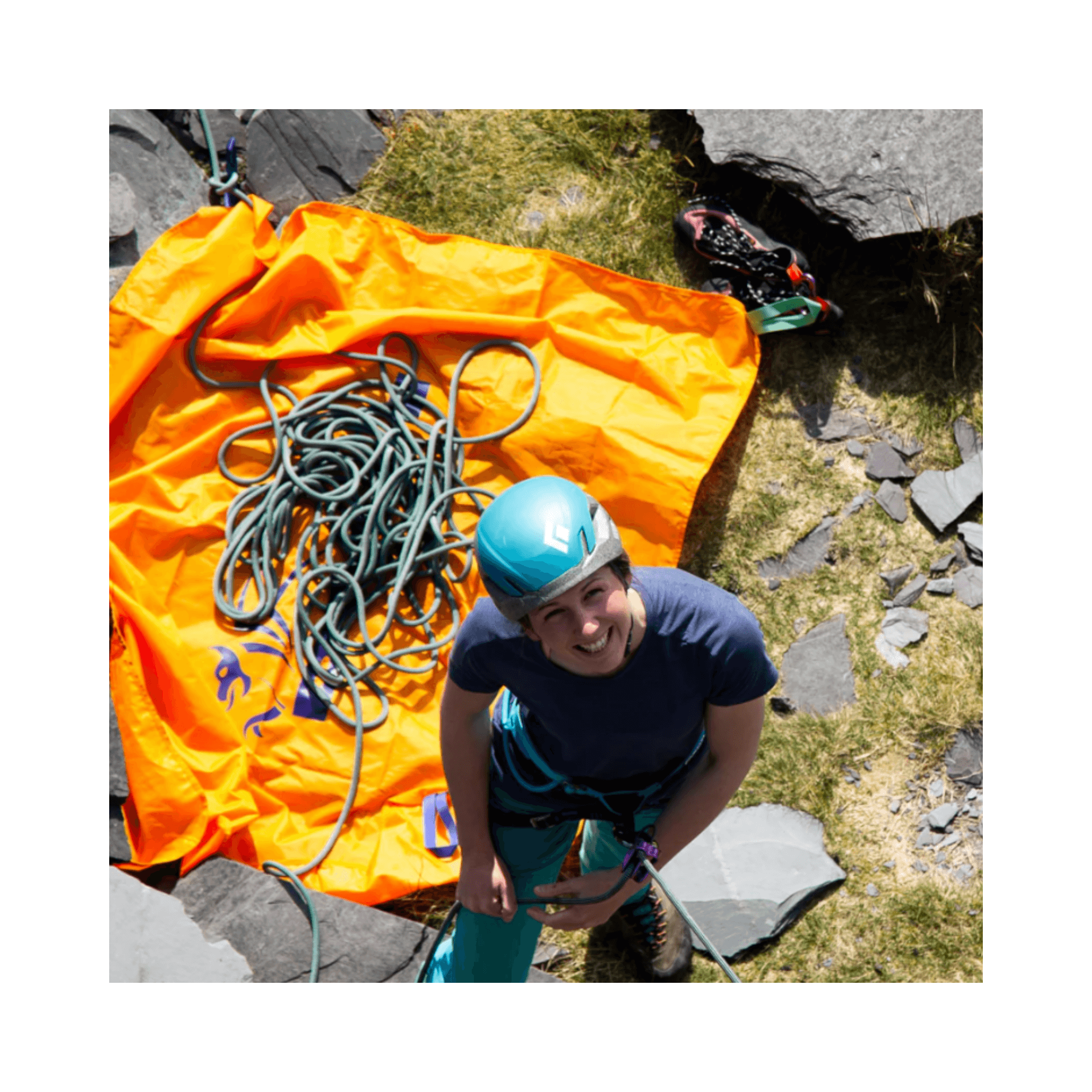 A climber smiling while standing on rocks near a DMM Classic Rope Bag 25L with a rope on an orange tarp.