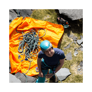 A climber smiling while standing on rocks near a DMM Classic Rope Bag 25L with a rope on an orange tarp.