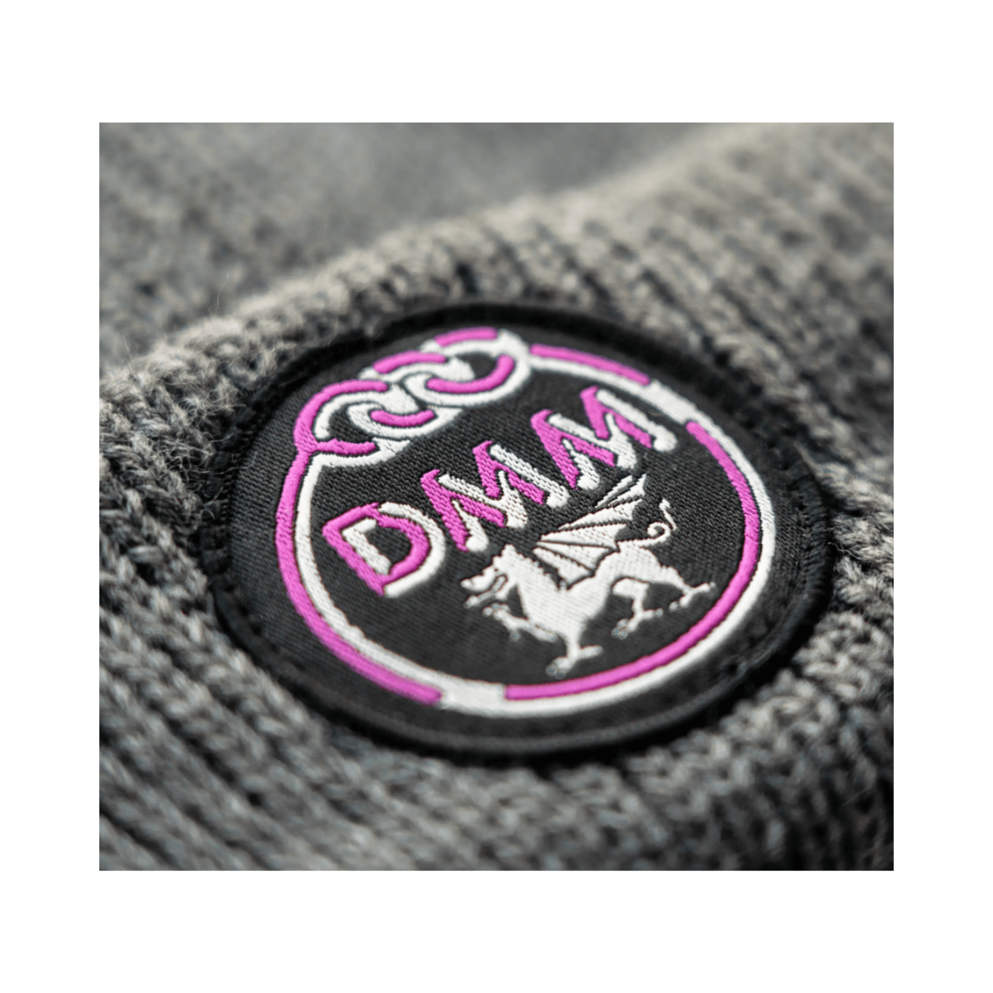 Close-up of the DMM logo on the Heritage Beanie in grey, featuring a pink emblem and craftsmanship for tree surgeons.