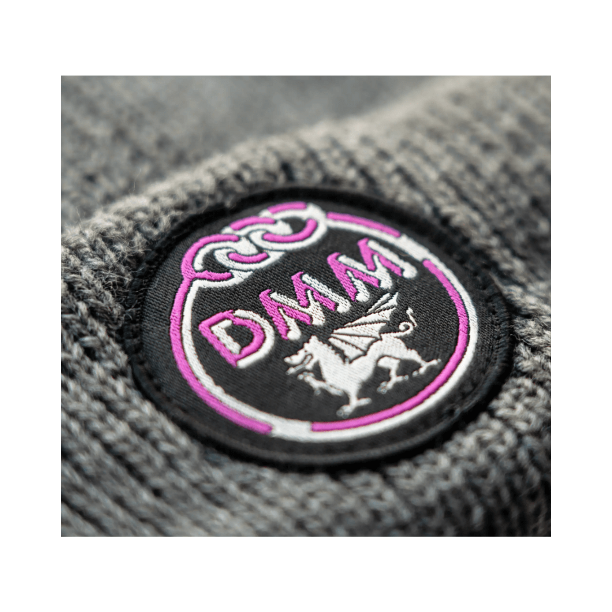 Close-up of the DMM logo on the Heritage Beanie in grey, featuring a pink emblem and craftsmanship for tree surgeons.