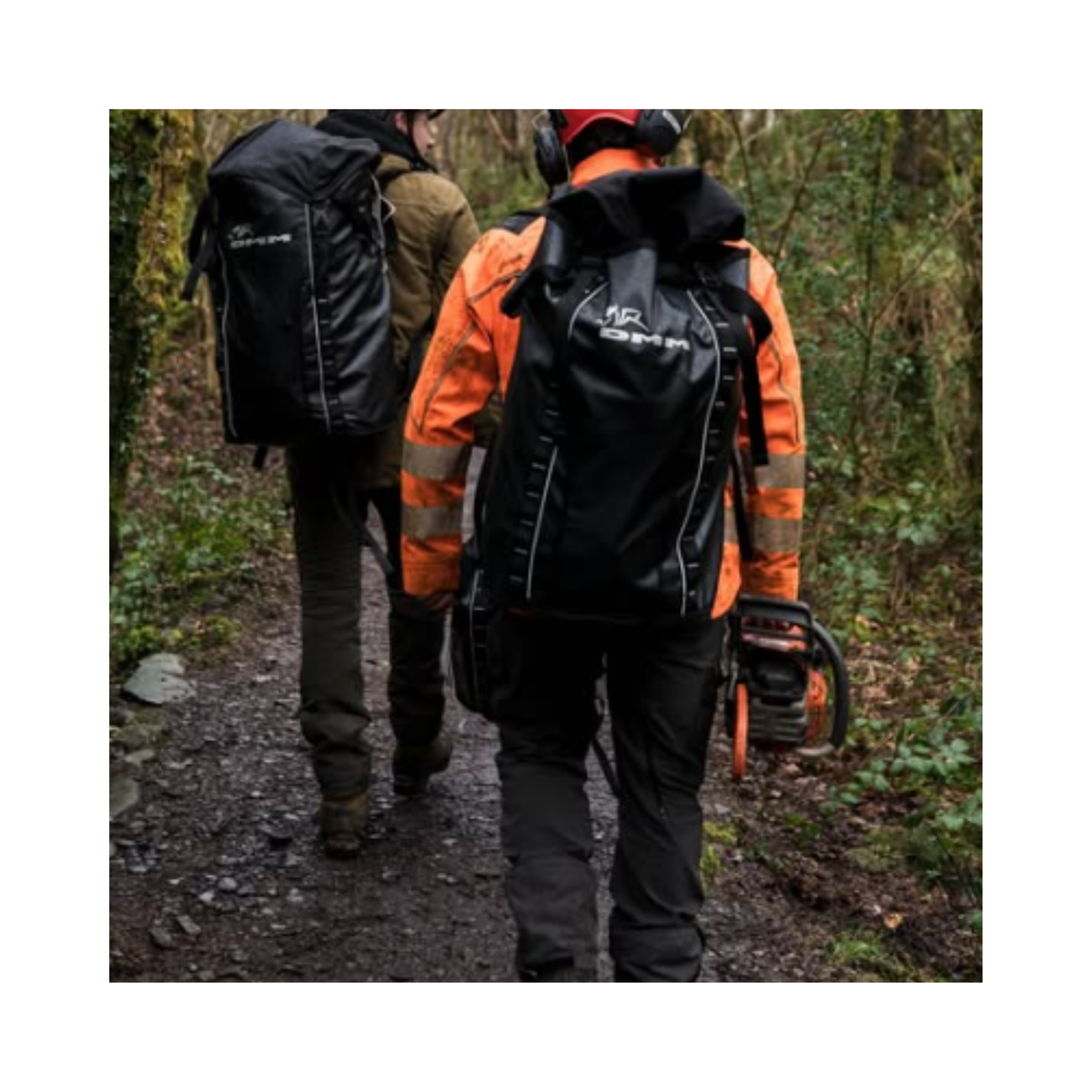 Two professionals carrying DMM Porter Rope Bags and a chainsaw on a wooded trail.