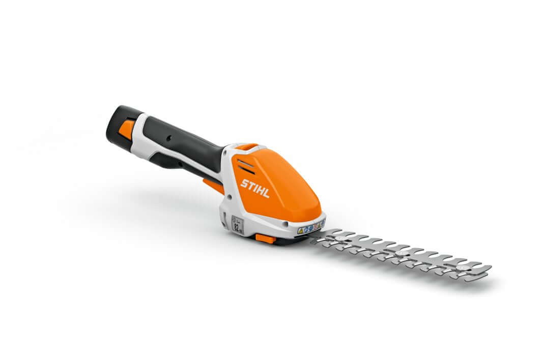 STIHL HSA 26 Cordless Shrub Grass Shears with interchangeable blades, a battery, and a charger, displayed alongside a black canvas storage case with the STIHL logo on it.