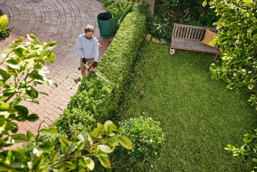 Man using HSA 40 cordless hedge trimmer to shape hedges in a well-maintained garden.