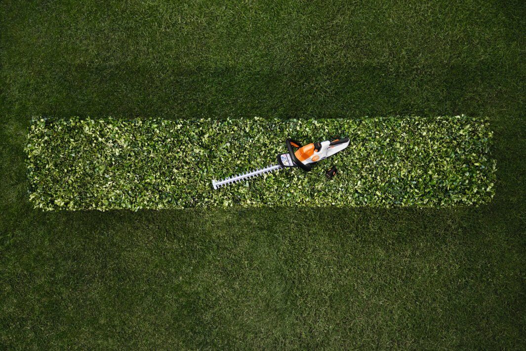 HSA 40 cordless hedge trimmer resting on neatly trimmed hedge, showcasing its lightweight design for tree surgeons.