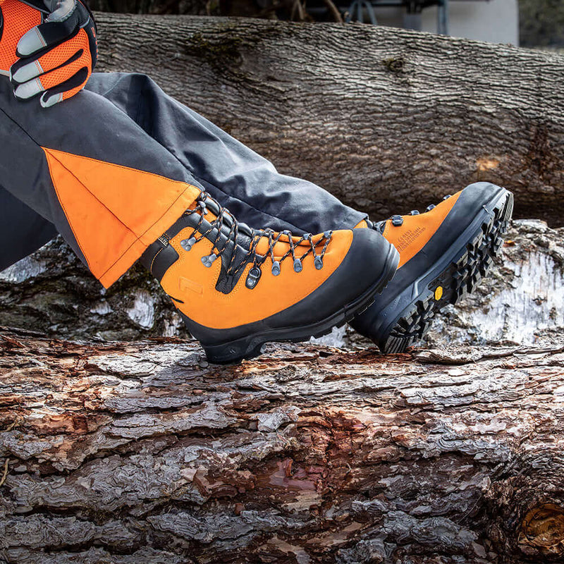 Close-up of rugged orange hiking boots on a log outdoors, showcasing durable design and grip for adventurous terrain.