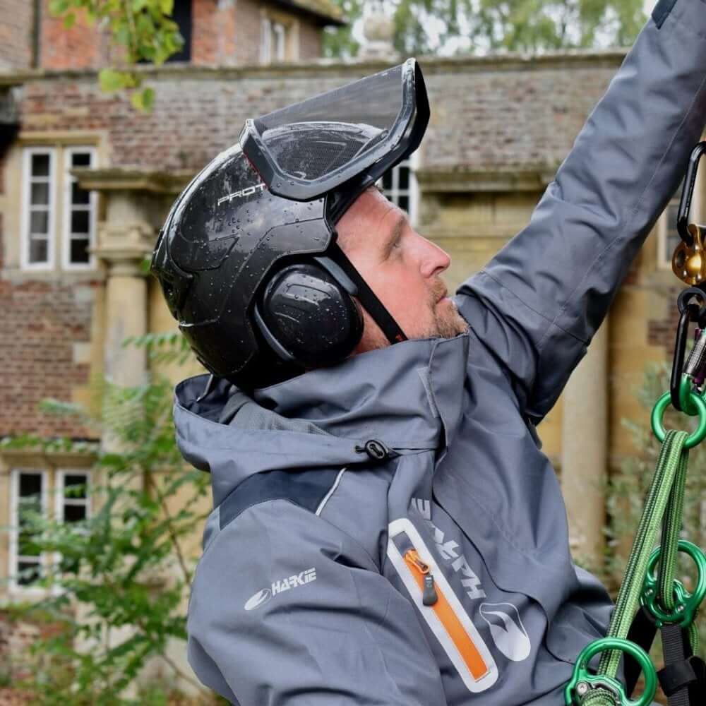 Tree surgeon wearing the Harkie Defiance Jacket Grey and a helmet, demonstrating outdoor workwear in action.