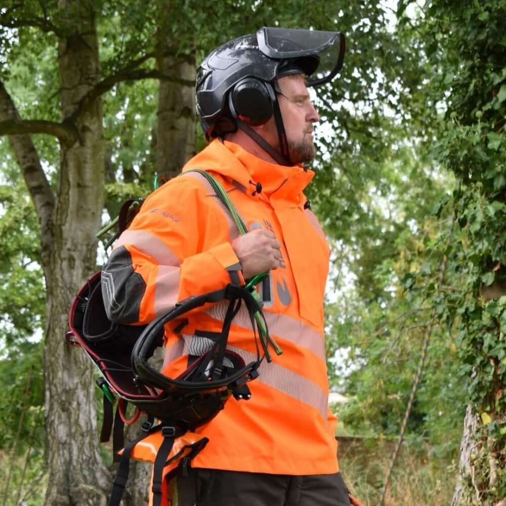 Tree surgeon wearing a Harkie Defiance Smock Hi Vis Orange in a forest, showcasing safety and durability for outdoor work.
