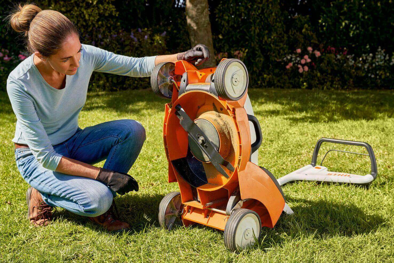 Woman maintaining a lawn mower in a garden, showcasing DIY lawn care and gardening tools.