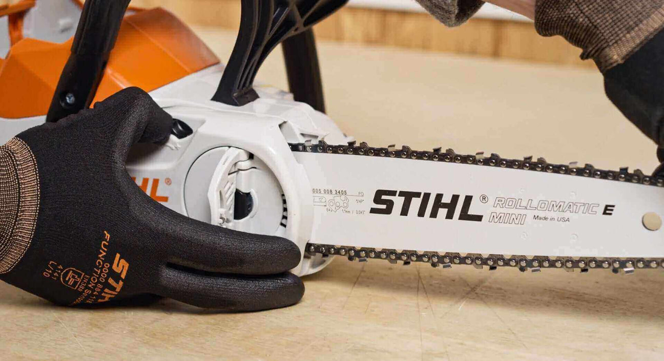 Close-up of a hand operating a STIHL chainsaw, showcasing the Rollomatic E Mini bar and chain.