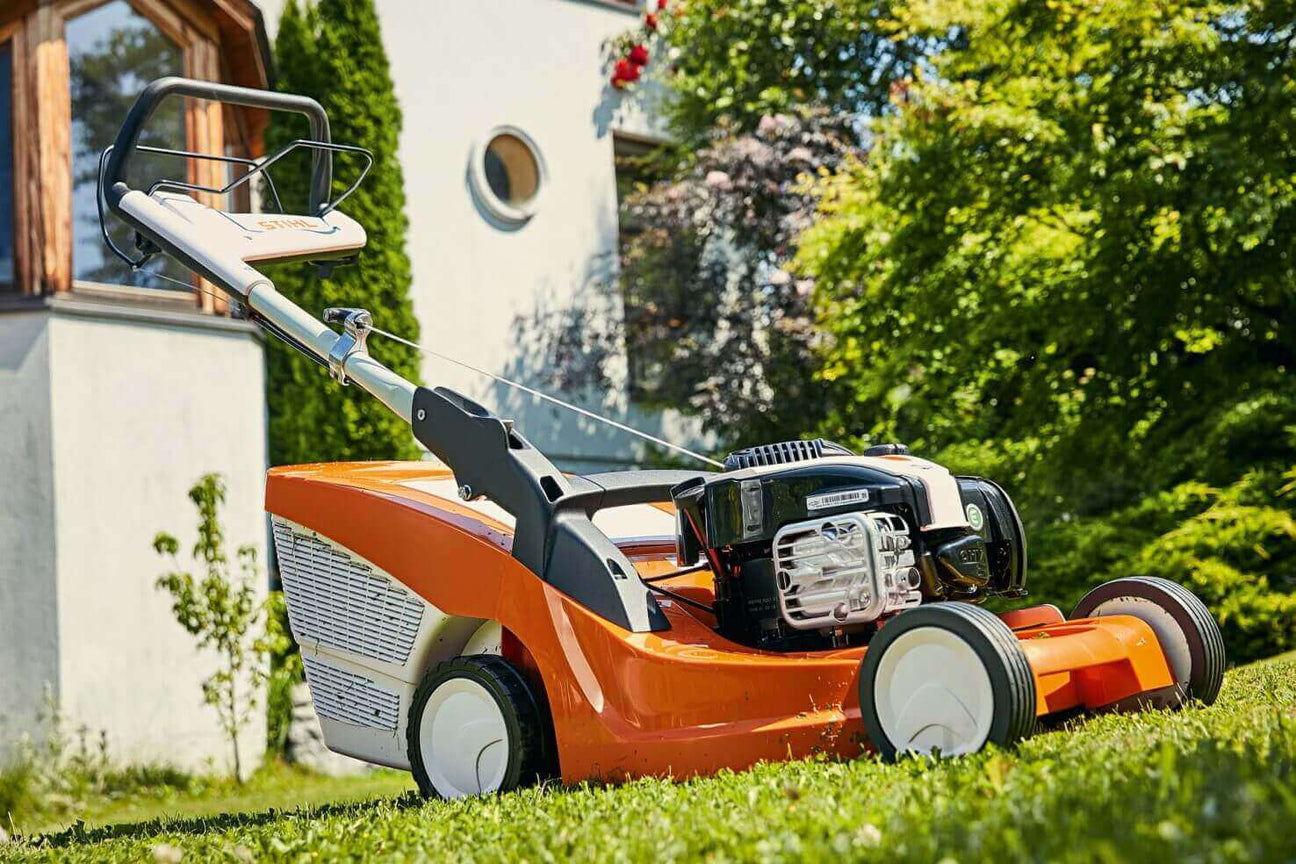 Lawn mower on grass in a garden setting, showcasing bright orange design and powerful engine.
