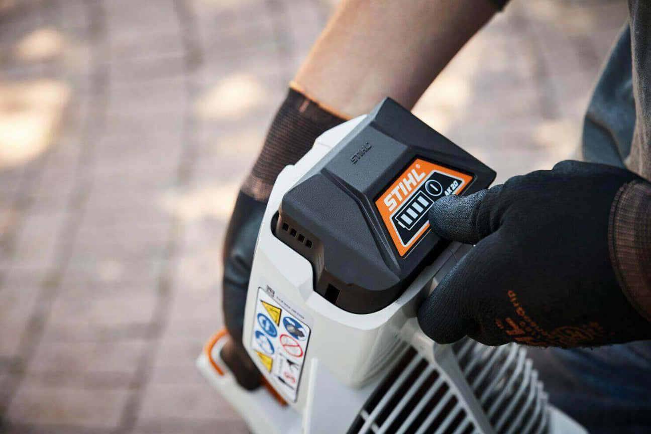 Close-up of a person wearing gloves adjusting the battery on a STIHL electric tool outdoors.