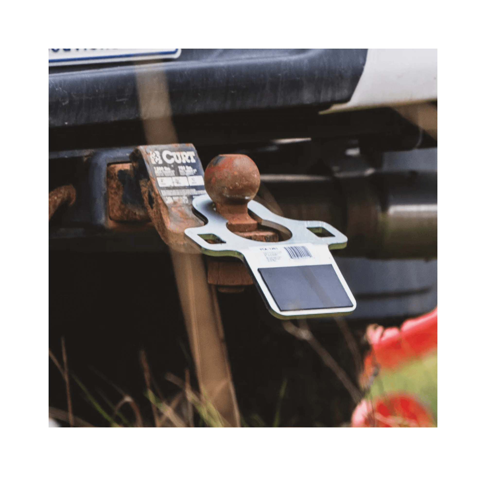 Tow hitch receiver on a vehicle with a visible brand label, surrounded by grass and flowers.
