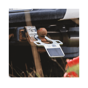 Tow hitch receiver on a vehicle with a visible brand label, surrounded by grass and flowers.