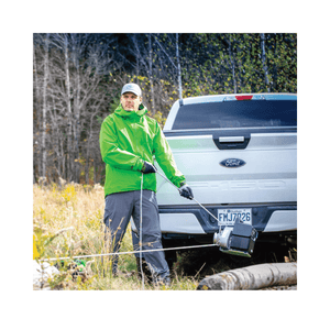 Man in green jacket using a winch anchor plate with a Ford truck in a forest setting.