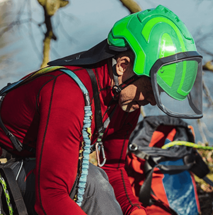 Climber wearing a green helmet and harness, preparing for outdoor adventure in a natural setting.