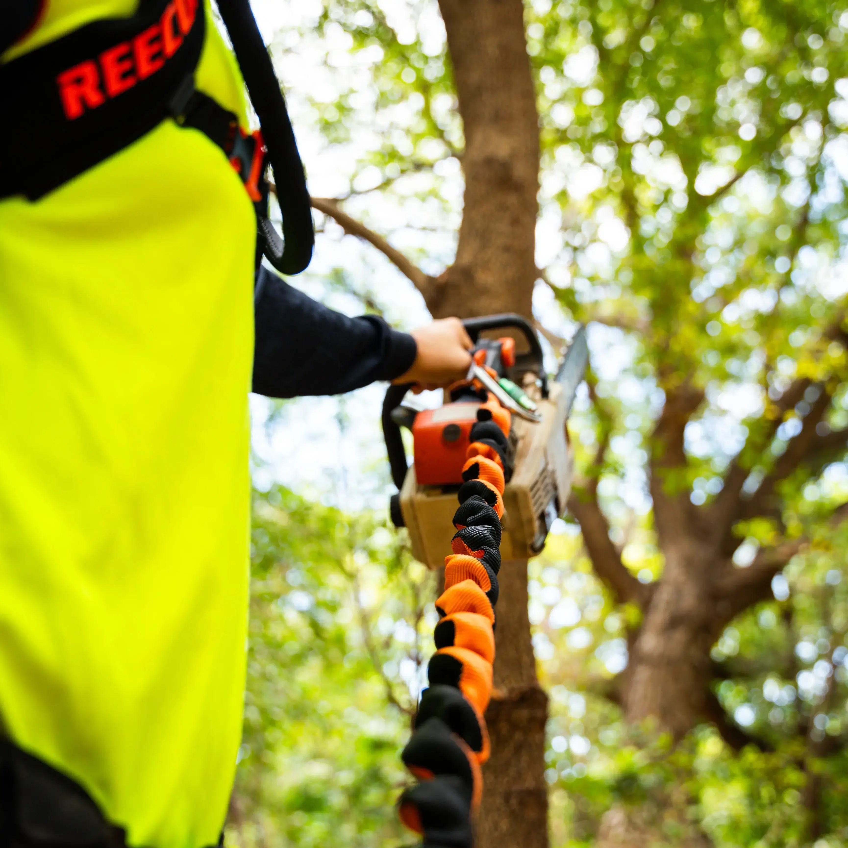 Tree surgeon using REECOIL Full-Reach chainsaw lanyard for mobility while cutting trees.