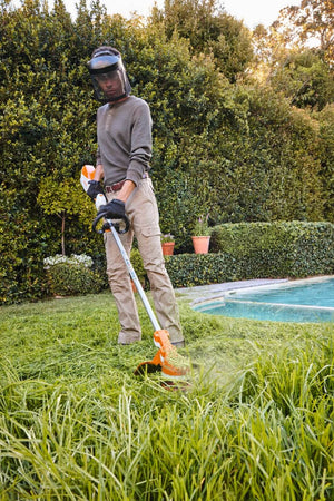 Professional using STIHL FSA 110 R cordless strimmer for landscaping near a pool in a garden.