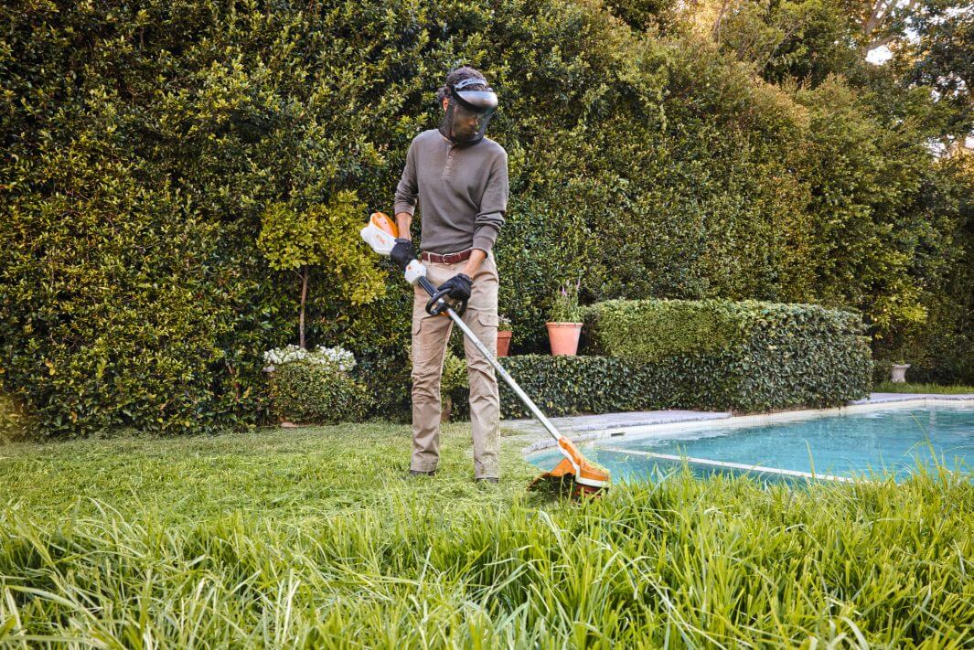 Professional using STIHL FSA 110 R cordless strimmer in a garden setting for quiet landscaping.