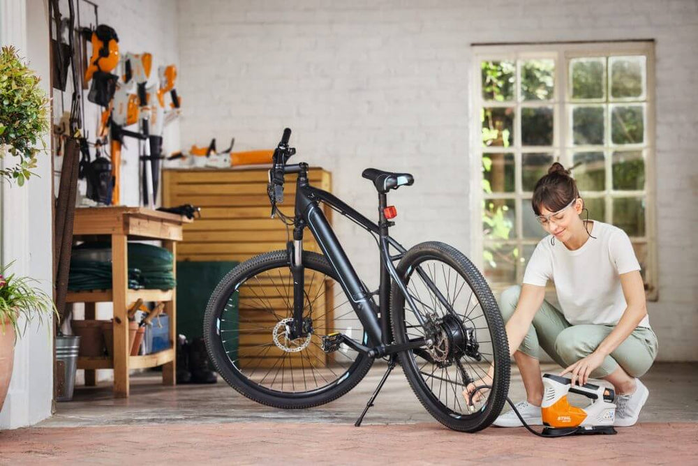 Woman using STIHL KOA 20 cordless compressor to inflate a bicycle tire in a garage setting.