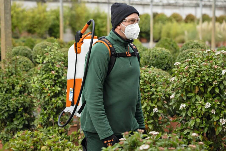 Tree surgeon using STIHL SGA 85 cordless backpack sprayer in a lush garden setting.