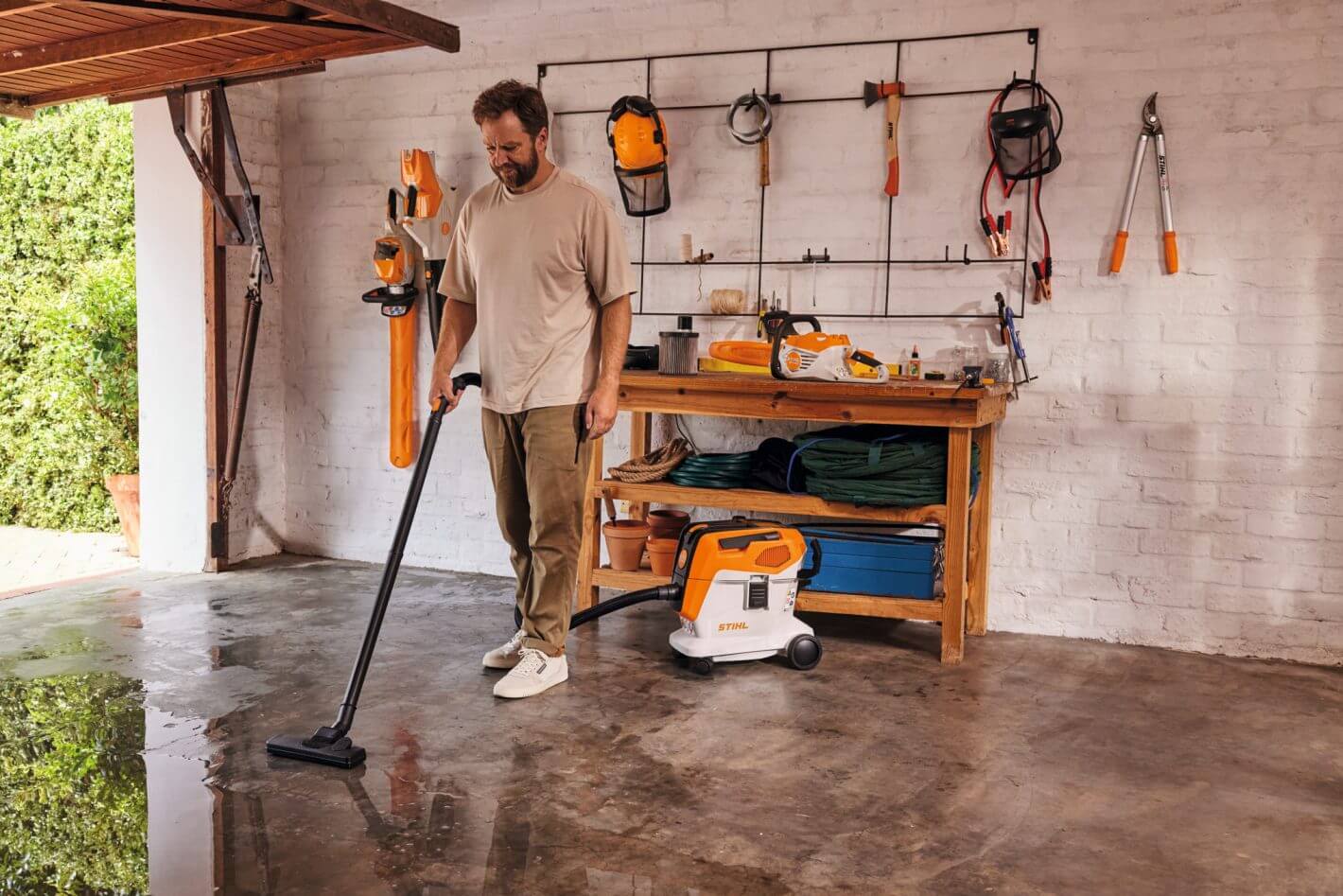 Man using STIHL SEA 60 cordless vacuum cleaner on wet floor in garage, showcasing powerful vacuum solutions for home and workshop.