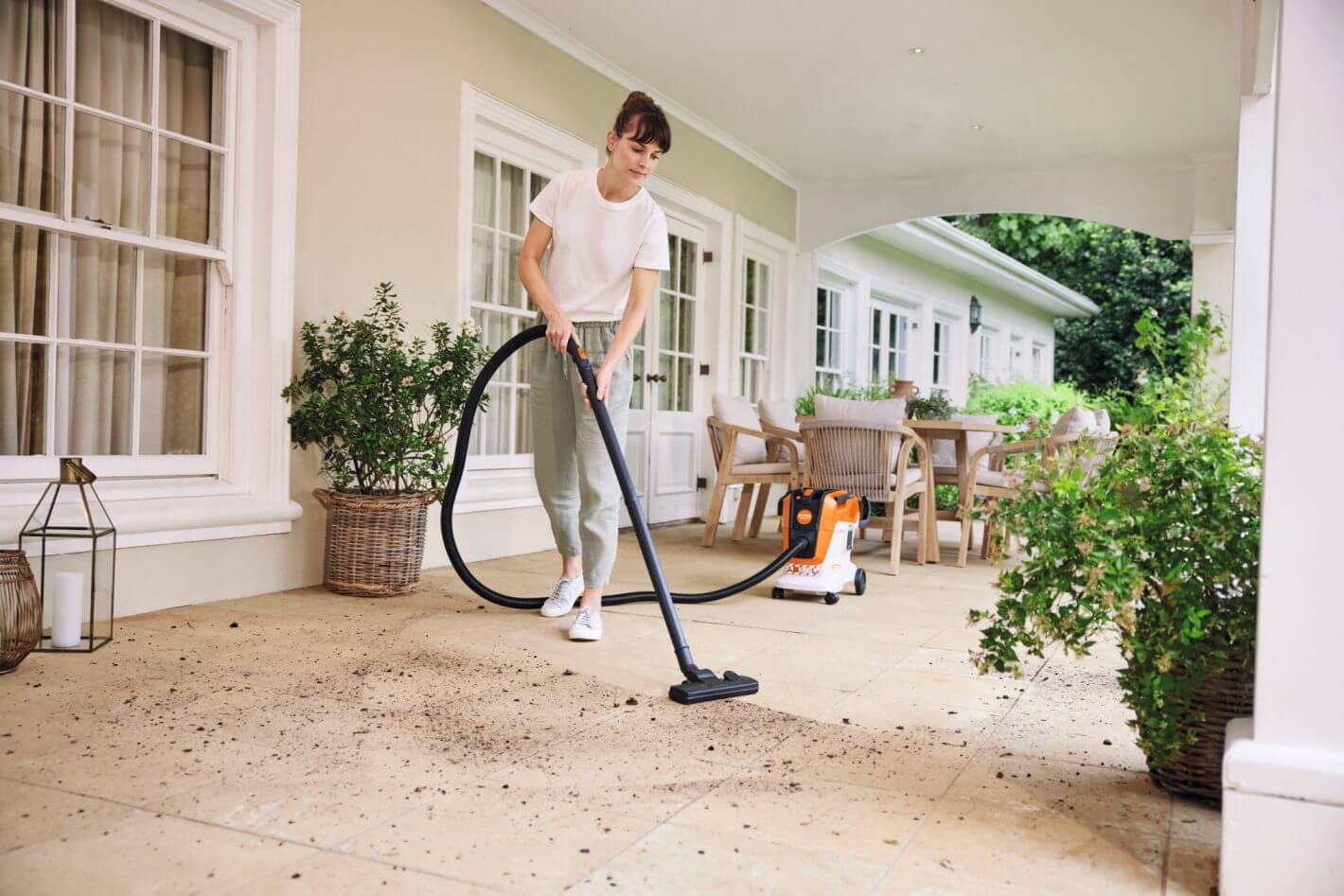 Woman using STIHL SEA 60 cordless vacuum cleaner on patio for effective cleaning.