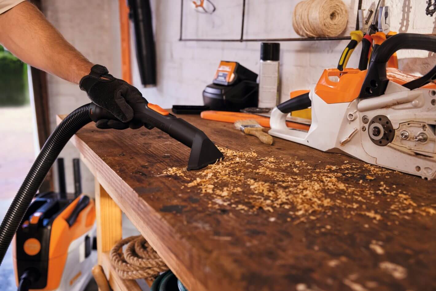 STIHL SEA 60 cordless vacuum cleaner in a workshop, efficiently cleaning sawdust from a wooden workbench.