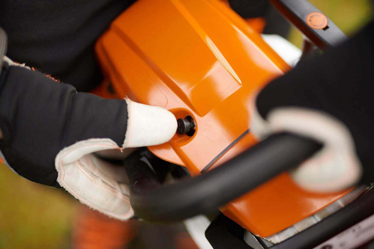 Close-up of a person adjusting a chainsaw, showcasing the orange body and gloves for safety.