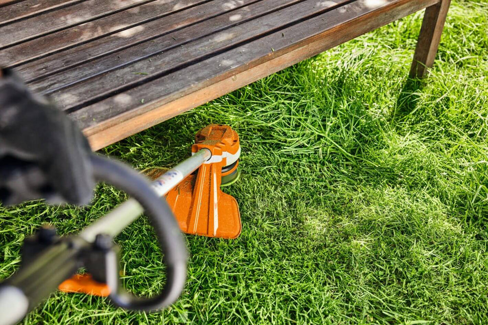 STIHL FSA 70 R cordless strimmer cutting lush grass under garden furniture in a home garden setting.