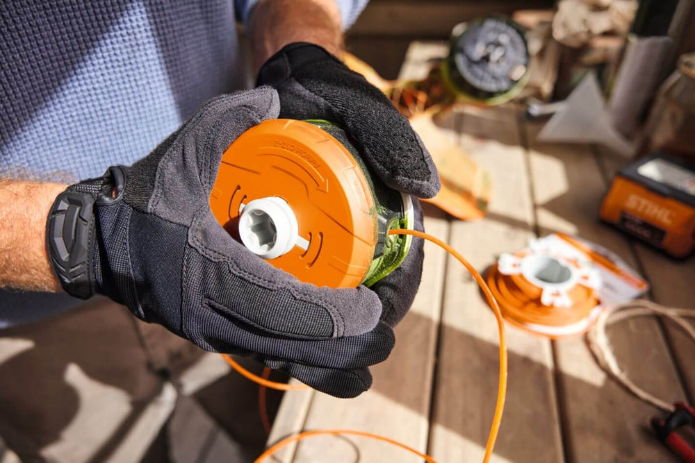 Person wearing gloves replacing spool on STIHL FSA 70 R cordless strimmer for effective garden maintenance.